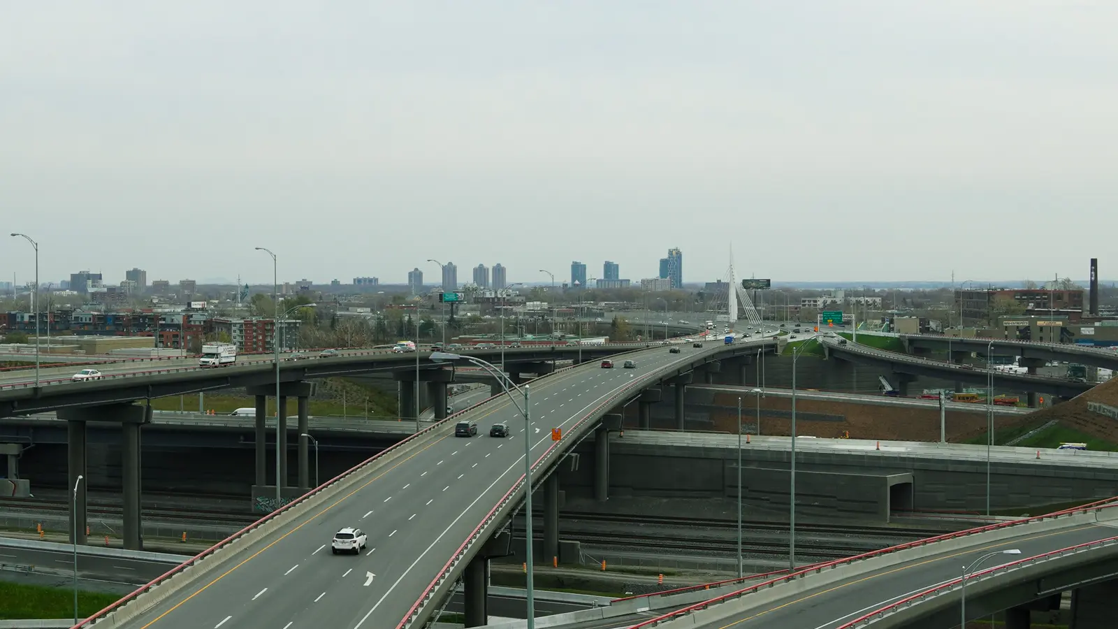 Trucks and cars crossing a highway interchange above a city skyline.